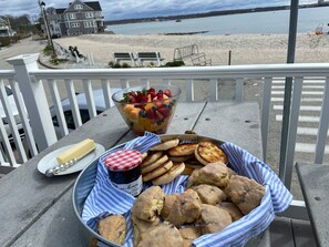 A table with a fruit salad, biscuits, butter, and jam on a balcony overlooking a beach. - Crescent Beach Cottage - Vacation or Academic Rental (Niantic)