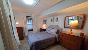 A bedroom with a bed, bedside tables, a dresser, a mirror, and a window with curtains. - Crescent Beach Cottage - Vacation or Academic Rental (Niantic)