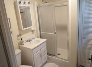 Une salle de bain avec un lavabo blanc, un miroir, des toilettes et une douche à parois de verre.