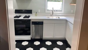 A compact kitchen with a gas stove, oven, dishwasher, and a window above the sink. - Crescent Beach Cottage - Vacation or Academic Rental (Niantic)