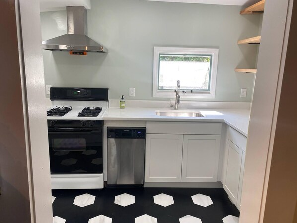 A compact kitchen with a gas stove, oven, dishwasher, and a window above the sink.