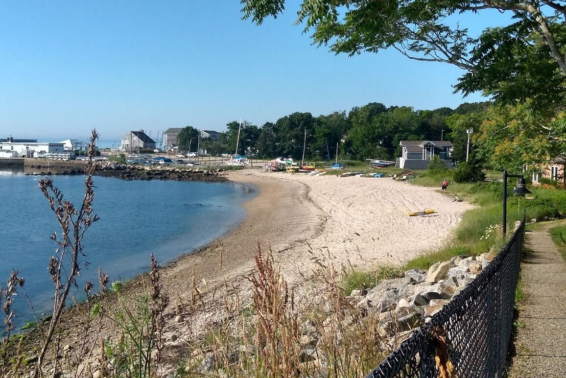 A beach with a sandy shore, a rocky breakwater, and a clear blue sky.