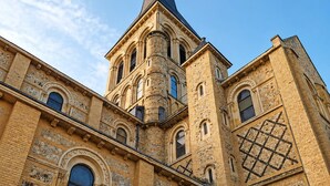 Un bâtiment historique doté d’une tour imposante, de fenêtres en arc de cercle et d’une porte rouge.