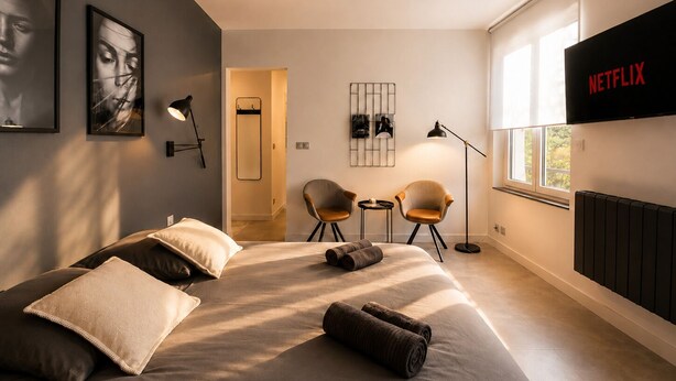 Une chambre moderne avec un lit, deux fauteuils, un téléviseur et des œuvres d’art accrochées aux murs.