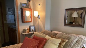 Une chambre d’hôtel avec un grand lit, une table de chevet avec une lampe, un miroir et une porte donnant sur une salle de bain.