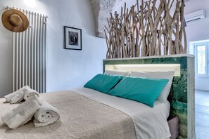 A bedroom with a bed, towels, a radiator, a picture, and a decorative wooden structure. - Sunsets over Ostuni and the sea - OSTUNI STYLE (Ostuni)