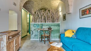 A room with a stone archway, a wooden desk with a chair, a blue sofa with a colorful pillow, and a rustic wooden cabinet. - Sunsets over Ostuni and the sea - OSTUNI STYLE (Ostuni)