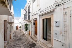 Une ruelle étroite pavée, bordée de bâtiments blancs dotés de balcons, de portes en bois et d’un compteur de gaz.