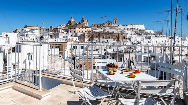 A rooftop terrace with white metal furniture, a table with a basket of fruits, and a view of a densely packed cityscape with white buildings. - Sunsets over Ostuni and the sea - OSTUNI STYLE (Ostuni)