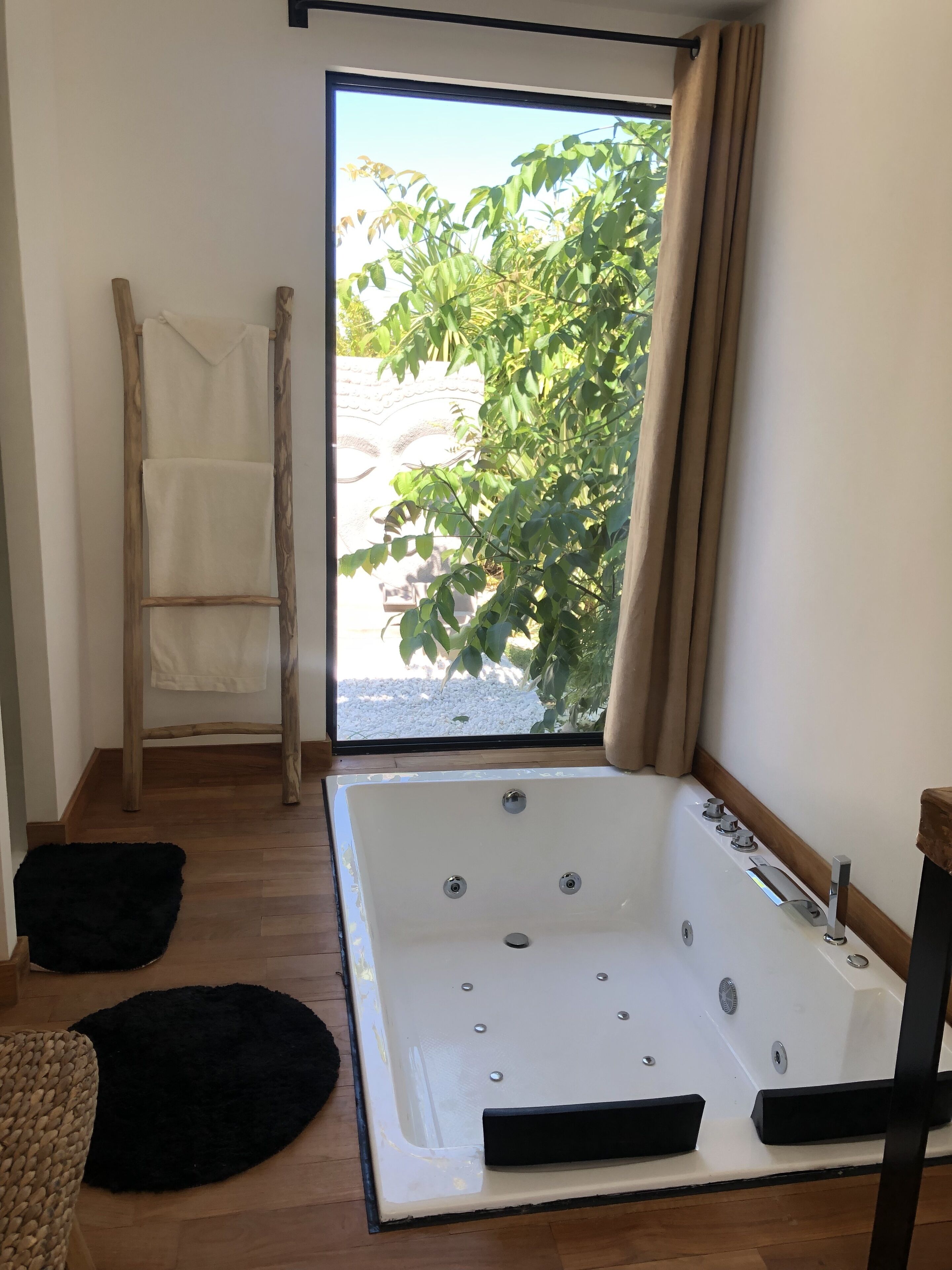 Un baño con una bañera grande, una escalera de madera y vistas al verdor exterior.