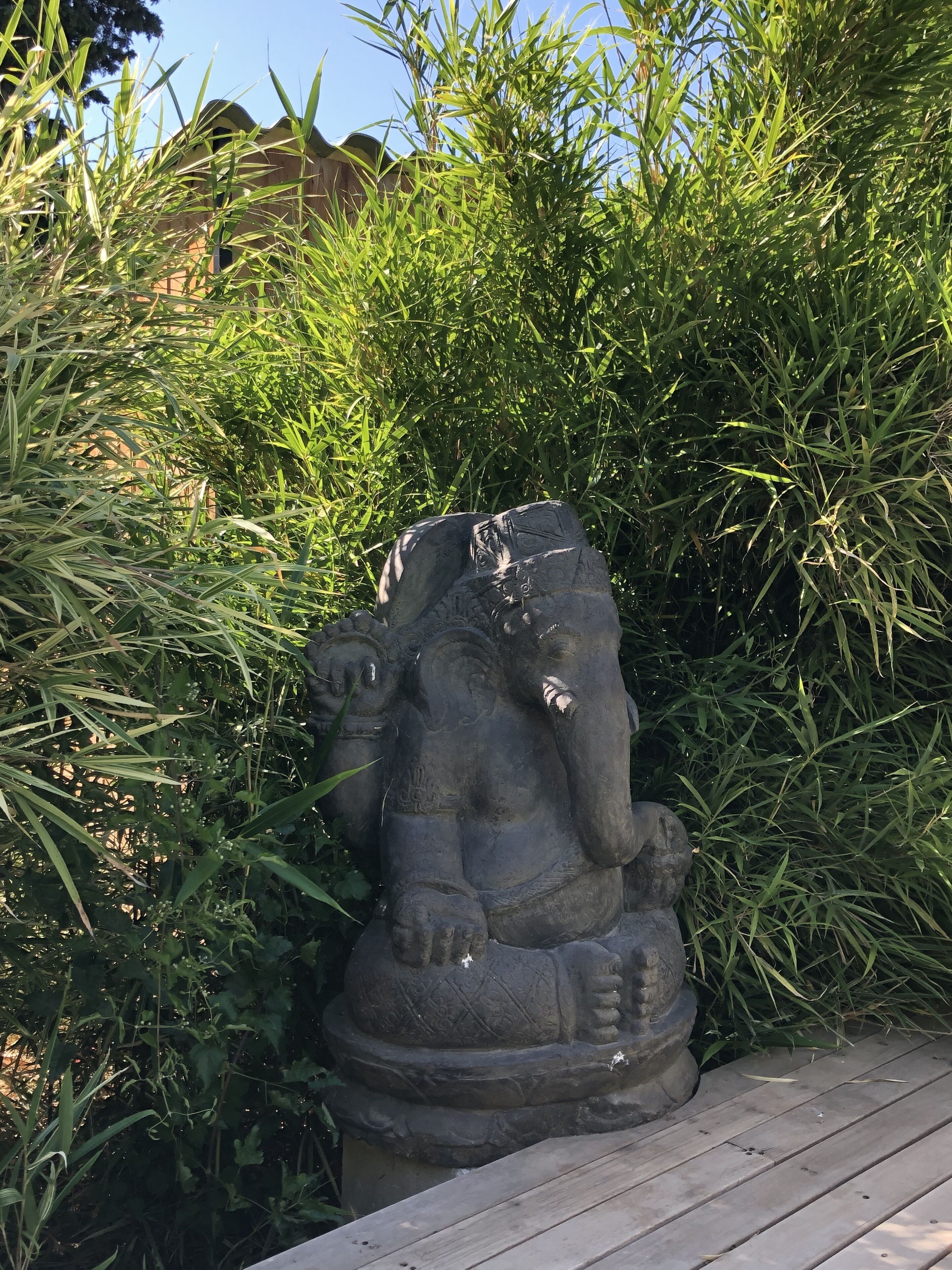 A stone elephant sculpture partially obscured by tall grass.