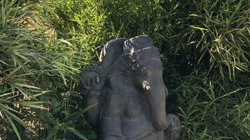 A stone elephant sculpture partially obscured by tall grass.