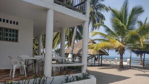 Een gebouw aan het strand met een terras, witte meubels en palmbomen.