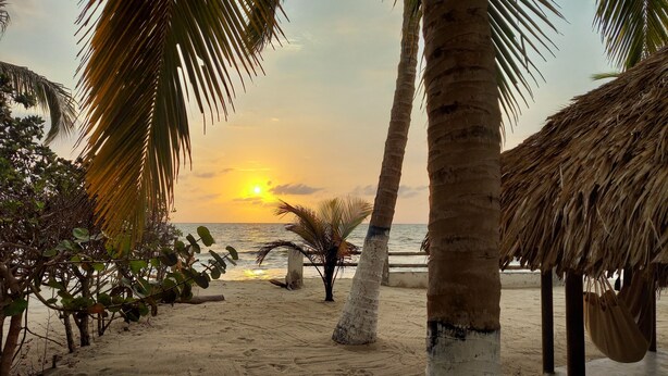 Een strandlandschap met palmbomen, een rieten hutje en een zonsondergang boven de oceaan.