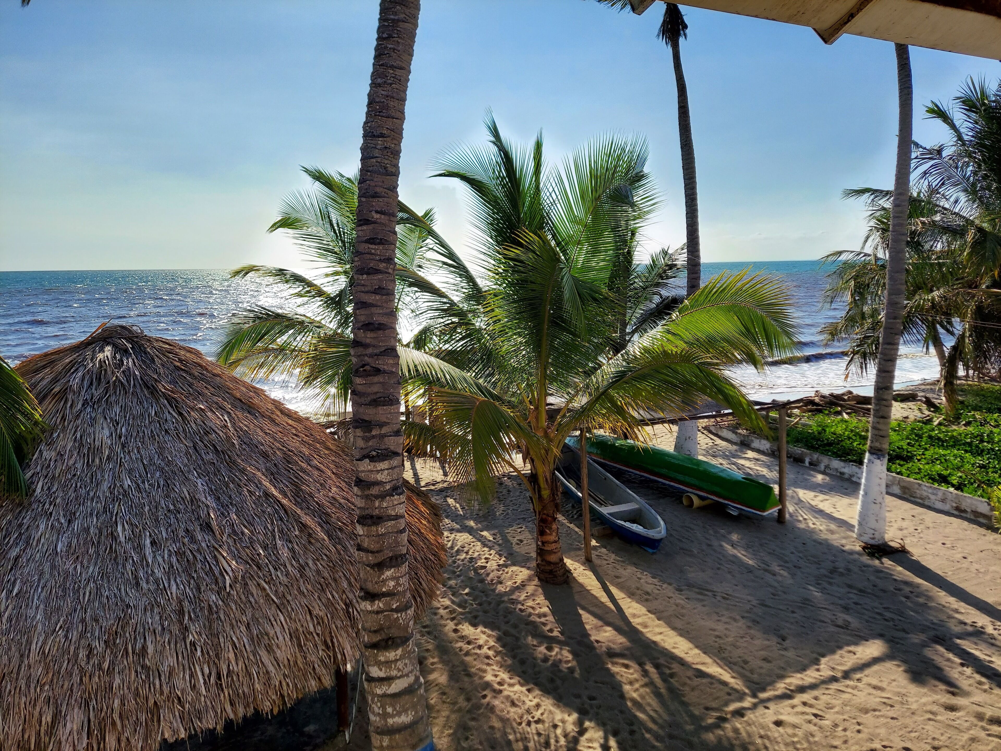 A beach scene with a thatched hut, palm trees, and a boat on the sand.