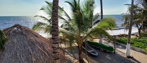 A beach scene with a thatched hut, palm trees, and a boat on the sand.