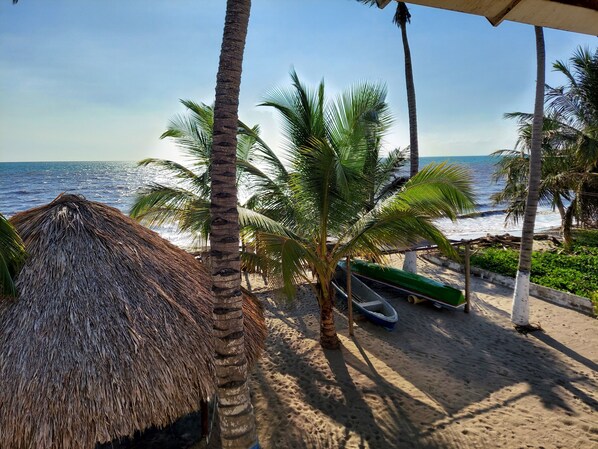 A beach scene with a thatched hut, palm trees, and a boat on the sand.