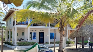 Een gebouw met twee verdiepingen en een balkon, omringd door palmbomen en boten op het strand.