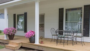 A porch with a wooden deck, a table with four chairs, and two large flower pots.