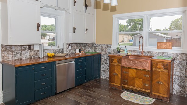 A kitchen with white cabinets, a copper sink, and a window with a view of houses.