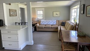 Een gezellige woonkamer met een beige bank, een houten eettafel en een keuken met witte kastjes.