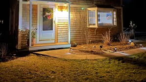 Een tweelaags huis met een kleine garage, een voortuin en een goed verlichte buitenkant bij nacht.