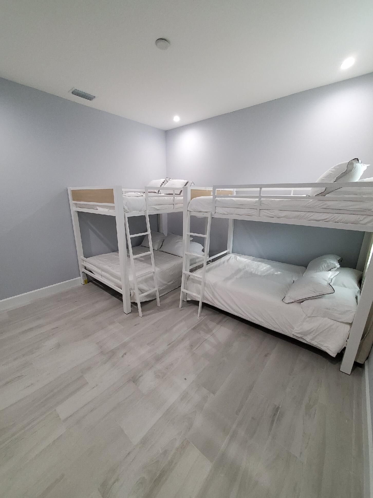 Una habitación con tres literas, piso de madera y techo blanco con lámpara.