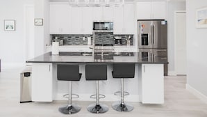 A modern kitchen with white cabinets, a black countertop, and three black bar stools. - Great reviews,Brand new,waterfront,heated pool, hot tub & beach access -14 pple  (Bonita Springs)