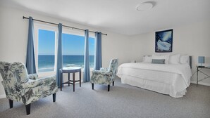 Une chambre d’hôtel avec un grand lit, deux fauteuils, une petite table et une vue sur l’océan.