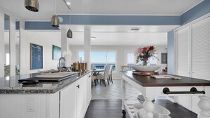 Une cuisine moderne avec des meubles blancs, un plan de travail en granit et une vue sur l’océan.