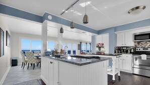 Une cuisine moderne avec des meubles blancs, un grand îlot central et une vue sur l’océan.