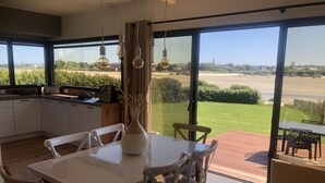 Eine moderne Küche mit großen Fenstern, einem Essbereich mit Tisch und Stühlen und Blick auf eine grüne Landschaft.