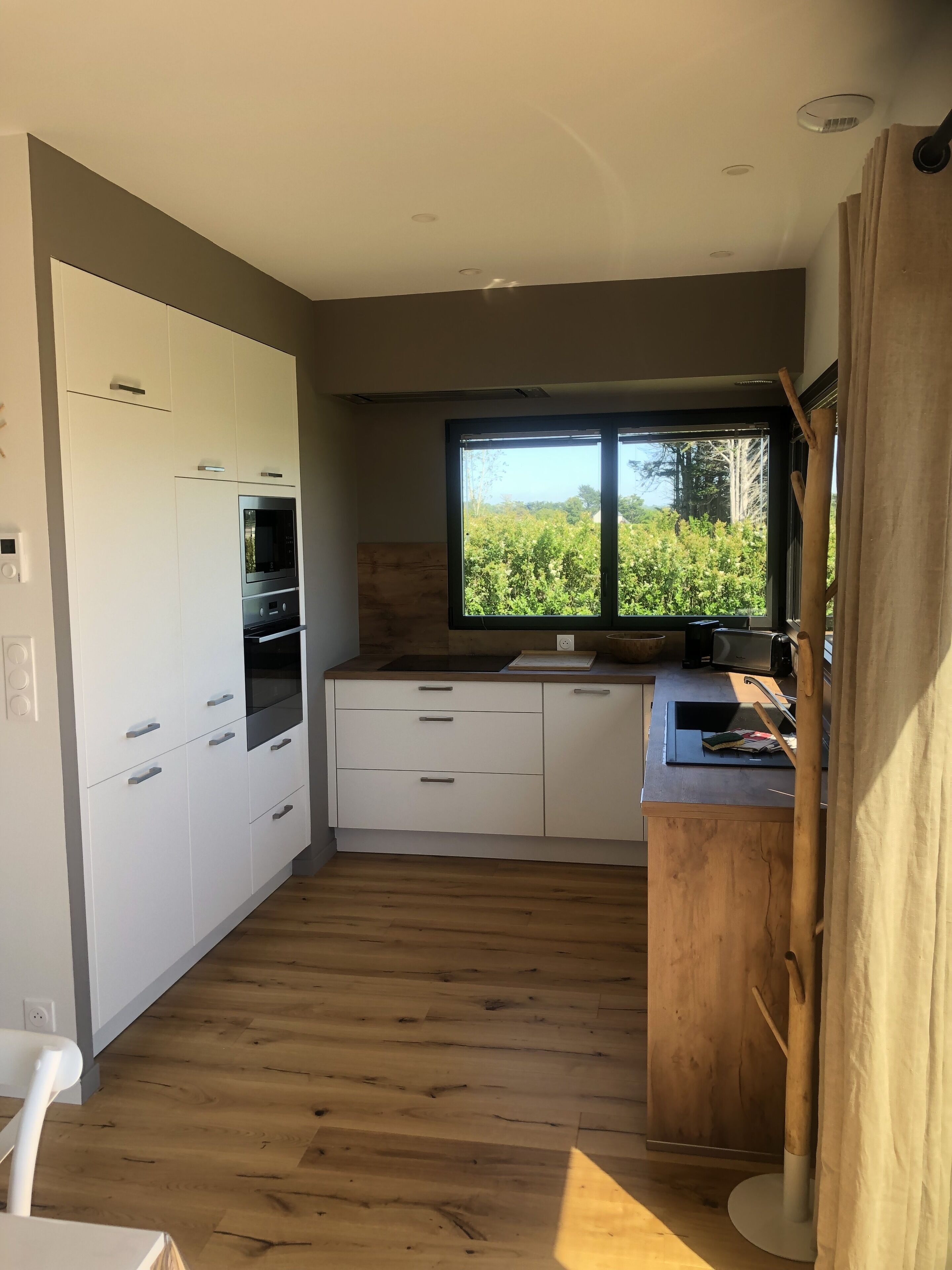 A modern kitchen with white cabinets, a built-in oven, and a window overlooking greenery.