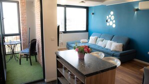 A modern living room with a blue accent wall, a blue sofa, and a kitchen area with a marble countertop. - New Modern Apartment With View in Omis, Croatia (Omis)