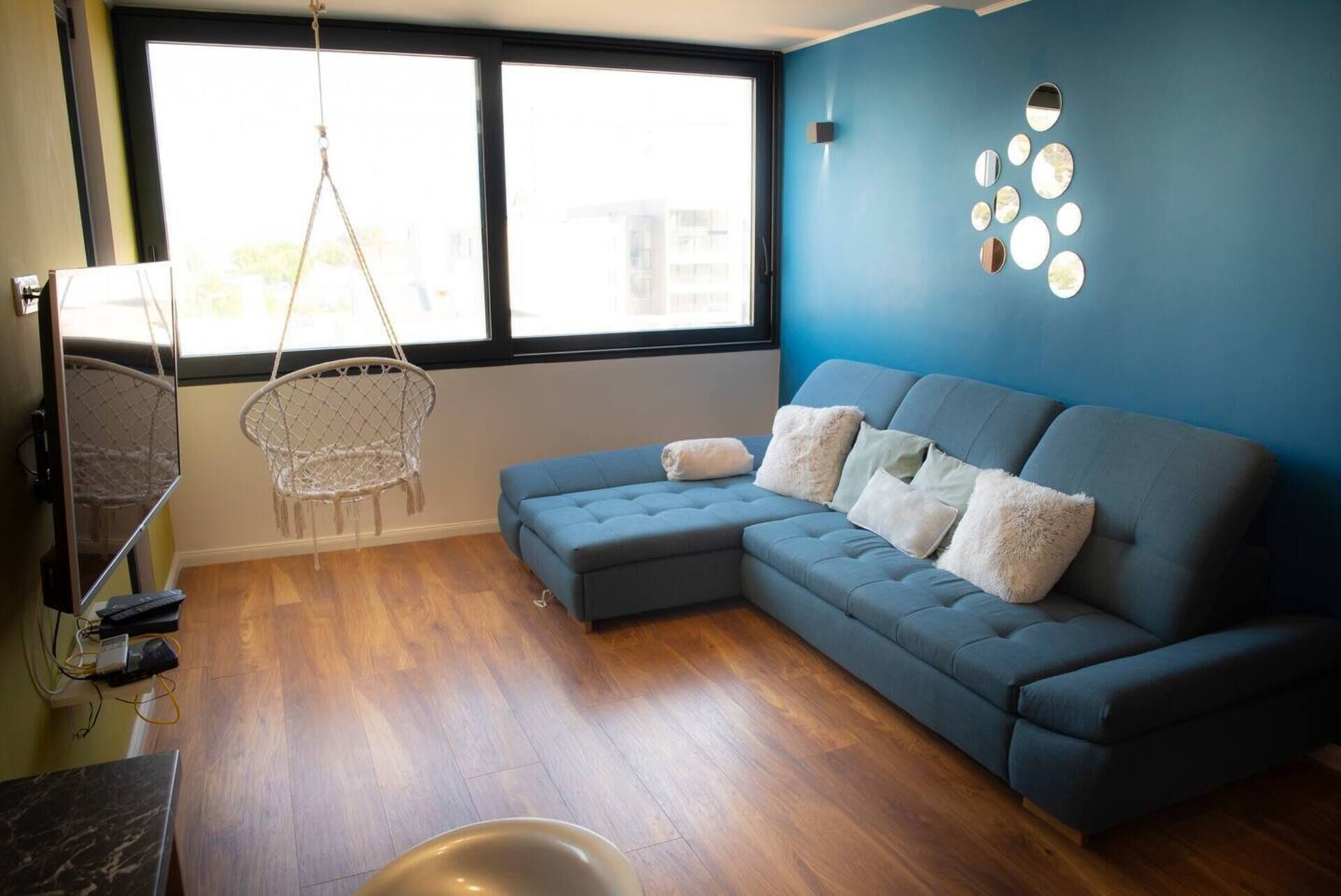 A modern living room with a blue sofa, a hanging chair, and a large window.