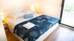 A neatly made bed with a dark blue blanket featuring nautical designs, white pillows, and a folded white towel. - New Modern Apartment With View in Omis, Croatia (Omis)