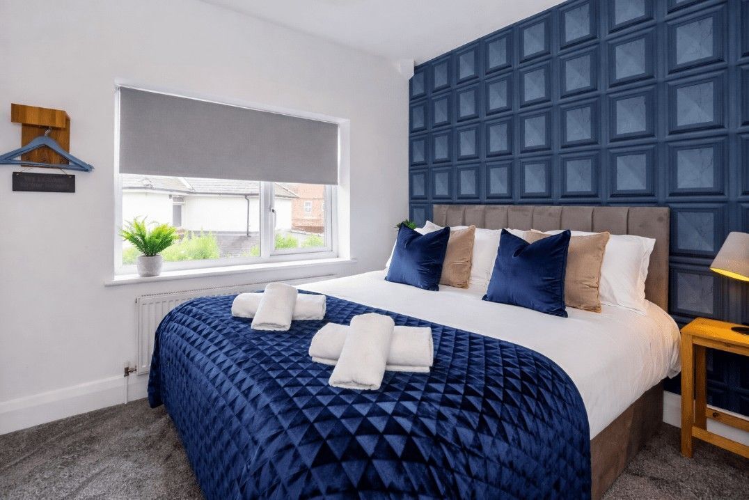 Ein Hotelzimmer mit einem großen Bett, einem Fenster mit Blick, einer blauen Wandverkleidung und einem kleinen Tisch mit einer Lampe.