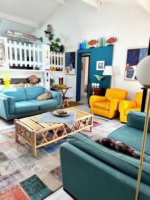 Un salon avec des canapés aux couleurs turquoise et jaune, une table basse en bois et des décorations représentant des poissons sur le mur.
