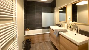 Un baño moderno con bañera, dos lavamanos, un espejo grande y una lámpara en el techo.