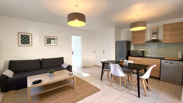 Una sala moderna con sofá, mesa de centro y comedor con sillas. Hay una cocina con refrigerador, microondas y alacenas.