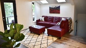 A living room with a red sofa and ottoman, a patterned rug, and a painting on the wall. - Relaxing Anchorage Retreat (Anchorage)