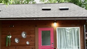 A wooden cabin with a red door, a window with a sheer curtain, and a small porch area with steps. - Relaxing Anchorage Retreat (Anchorage)