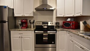 A kitchen with white cabinets, a stainless steel refrigerator, a red coffee maker, a microwave, and a stove. - Relaxing Anchorage Retreat (Anchorage)