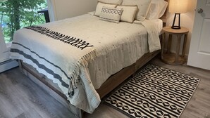 A bedroom with a wooden headboard, a bed with a striped blanket, multiple pillows, a bedside lamp, and a patterned rug. - Relaxing Anchorage Retreat (Anchorage)