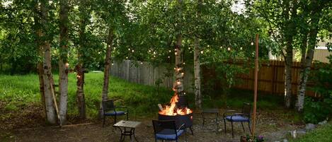 An outdoor patio area with a fire pit, two metal chairs, and a table.