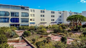 A modern building with multiple floors, large windows, and a courtyard with various plants and a pathway.