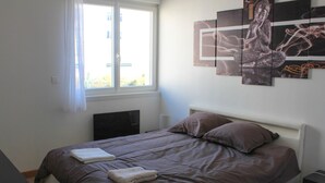 A bedroom with a bed, pillows, a window with curtains, and wall art.