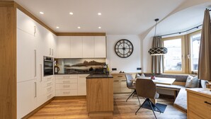 A modern kitchen with wooden cabinets, a central island, and a dining area with a bench. - Apartments Fina 158A (Ortisei)