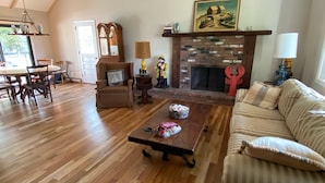 A spacious living room with a high ceiling, wooden flooring, a fireplace, a sofa, a coffee table, and a dining area with chairs and a table. - Harwich home close to the beach (Harwich)