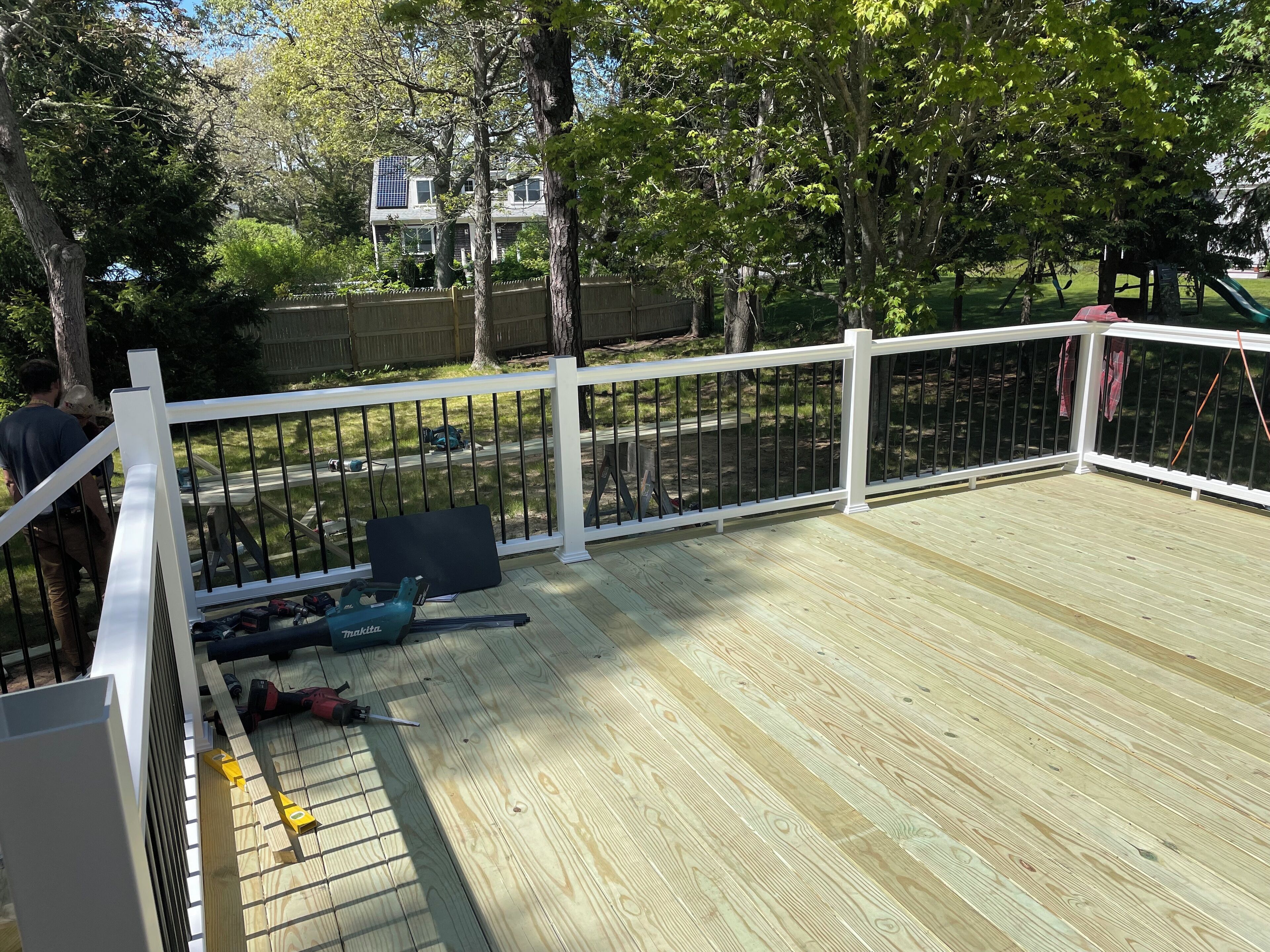 A wooden deck with a white railing, construction tools, and a partially built fence.